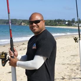 A man standing on the beach beside fishing poles wearing IceRays Sun Sleeves for Maximum sun protection while fishing. Fishing 